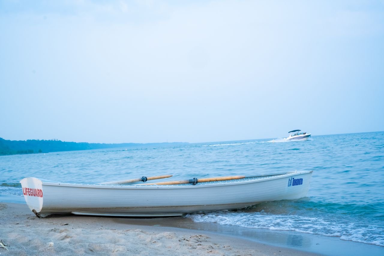 our-stories A lifeguard boat rests on a sandy Toronto beach with a distant motorboat on a summer day.